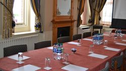 Elegant conference room with a large table set for a meeting, featuring bottled water, glasses, notepads, and decorative curtains.