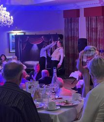 Dinner theater scene with performers on stage and audience seated at tables.