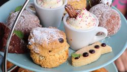 Assorted pastries and desserts on a blue tiered tray, including cream-topped cups, scones, brownies, and shortbread.