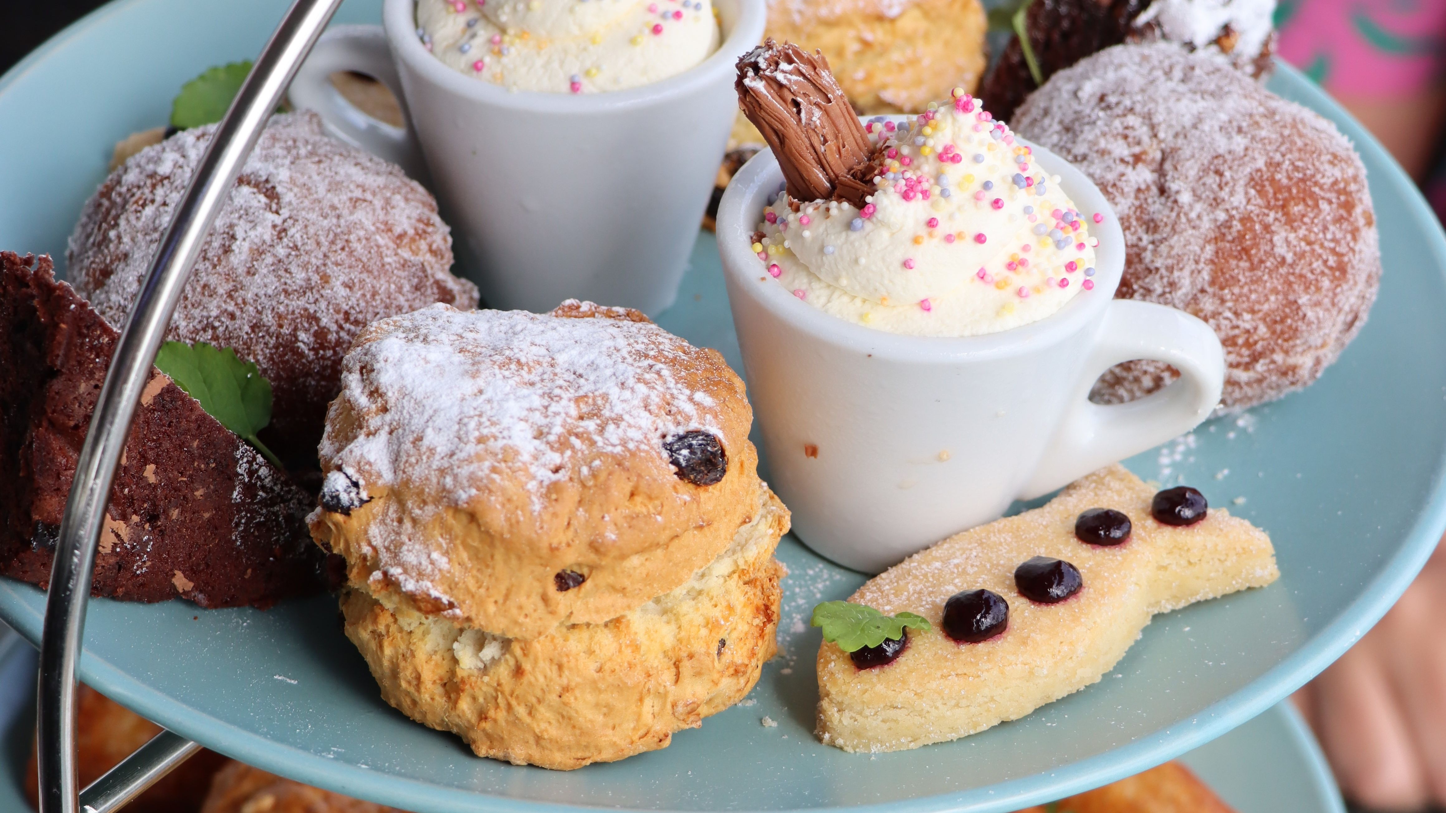 Assorted pastries and desserts on a blue tiered tray, including cream-topped cups, scones, brownies, and shortbread.