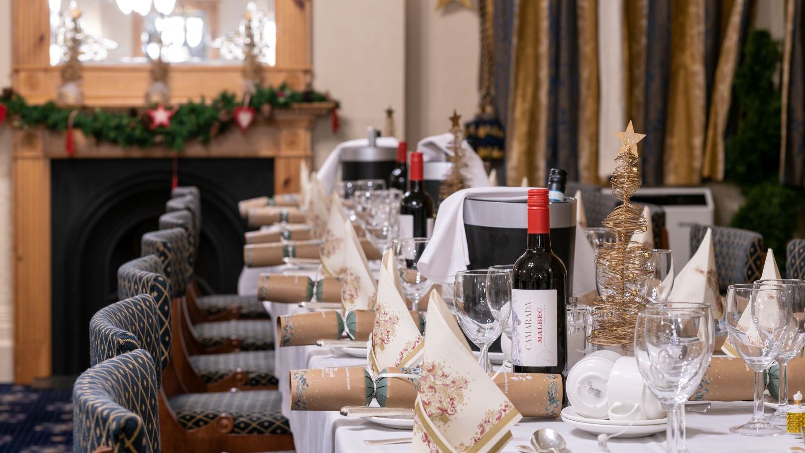 Elegant dinner table setup at a hotel with festive decorations, wine bottles, crackers, and folded napkins.