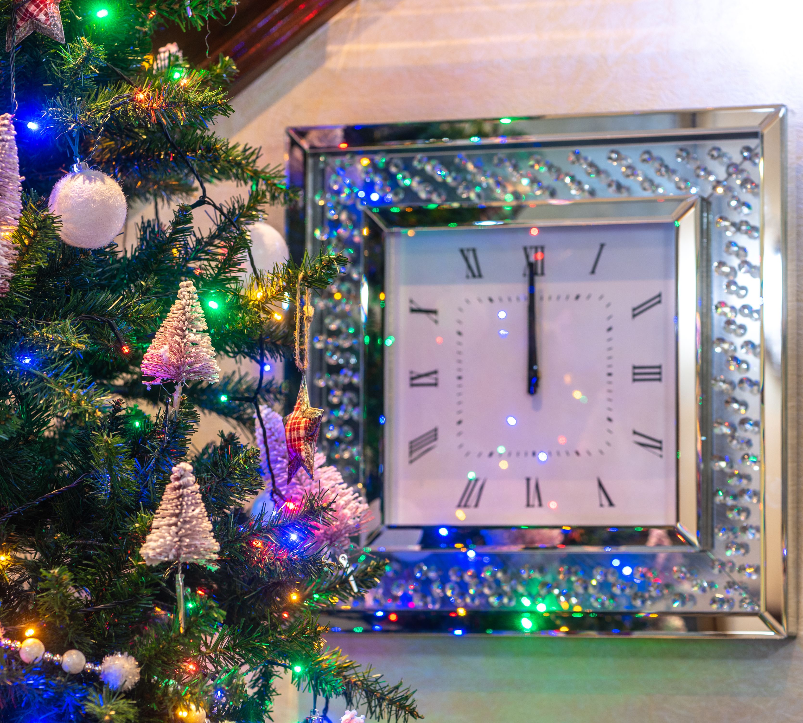 Decorated Christmas tree next to a wall clock striking midnight