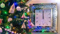 Decorated Christmas tree next to a wall clock striking midnight
