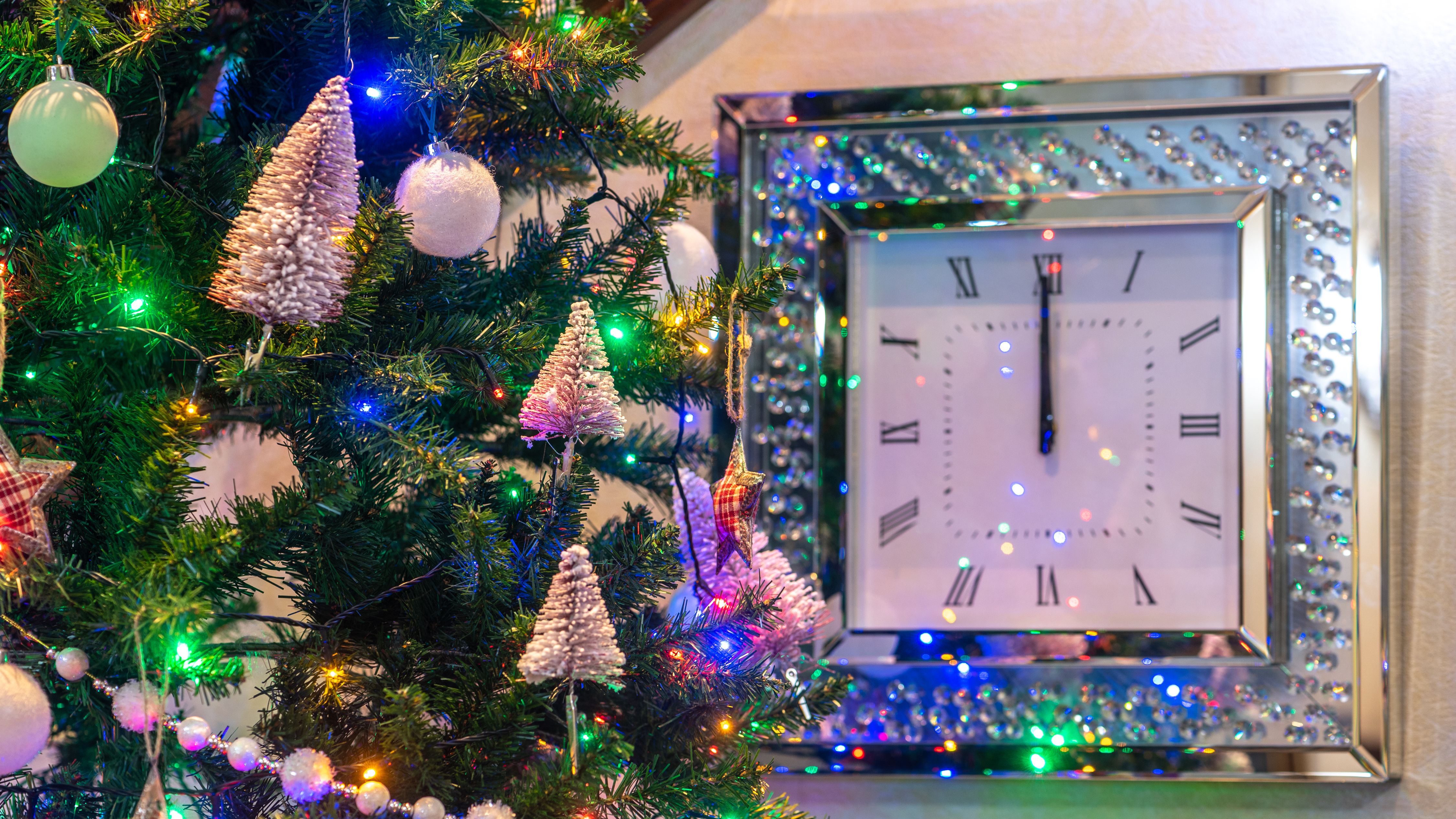 Decorated Christmas tree next to a wall clock striking midnight