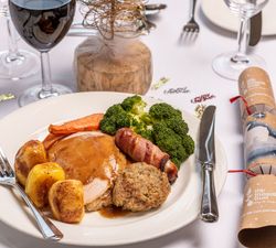 A traditional Christmas roast dinner with turkey, roast potatoes, vegetables, and stuffing, served with gravy on a white plate.