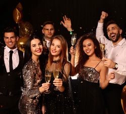 Group of young adults celebrating with champagne at a party with gold balloons and confetti.