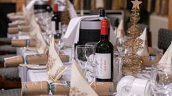 A festive dining table set with wine, glasses, Christmas crackers, napkins, and gold wire Christmas tree decorations.