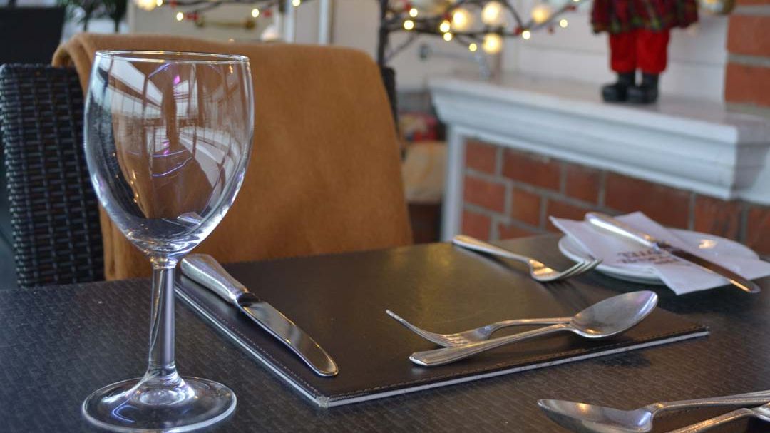 A restaurant table set for dining with a wine glass, cutlery, and a menu, with festive lights and a Santa Claus decoration in the background.