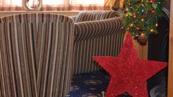Cozy living room with striped furniture, a large red star decoration, and Christmas garland with lights on the fireplace.
