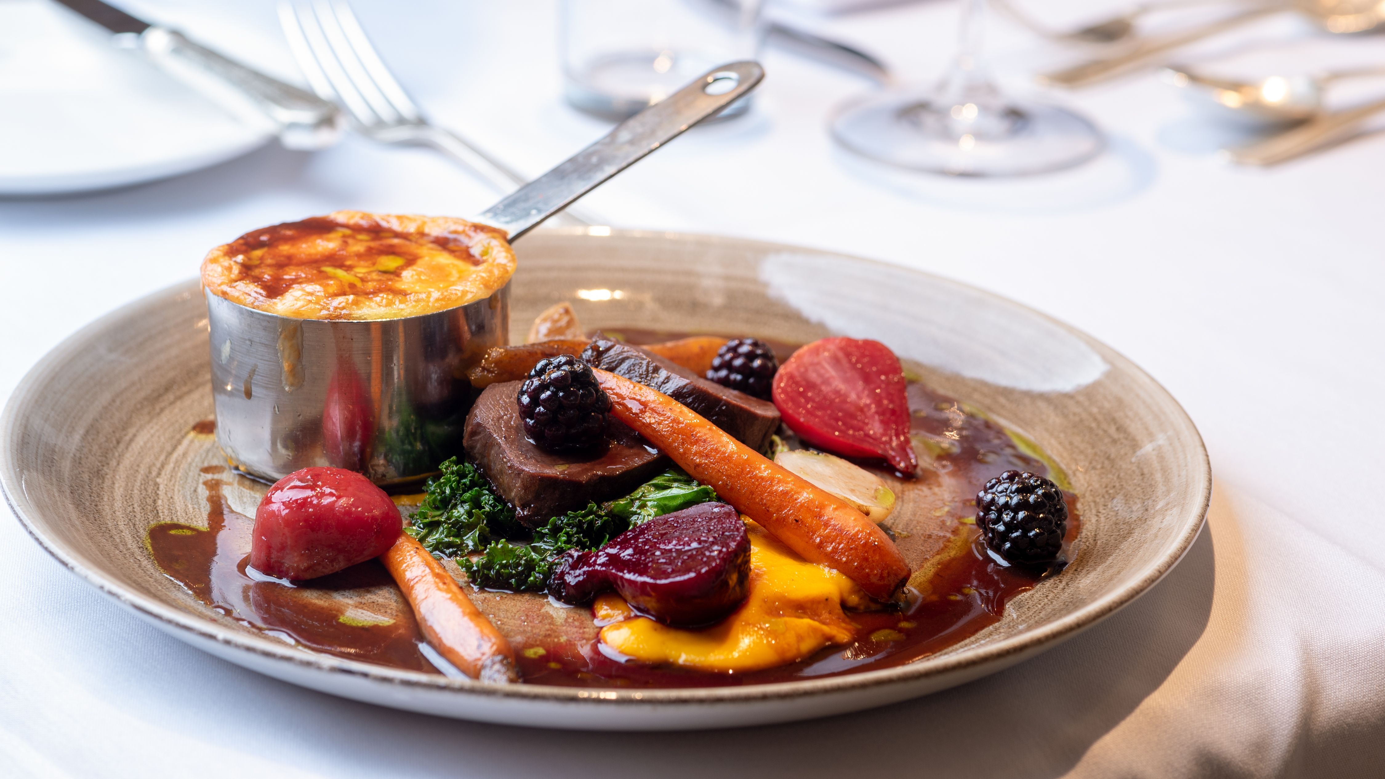 Gourmet plated main course with vegetables, sauce, and a small baked dish on a restaurant table.