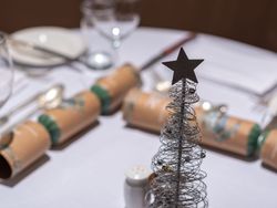 A decorative wire Christmas tree with a star topper on a festive dining table set with crackers, glassware, and cutlery.