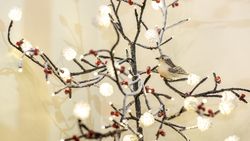 Decorative bird perched on a festive branch with lights and faux berries