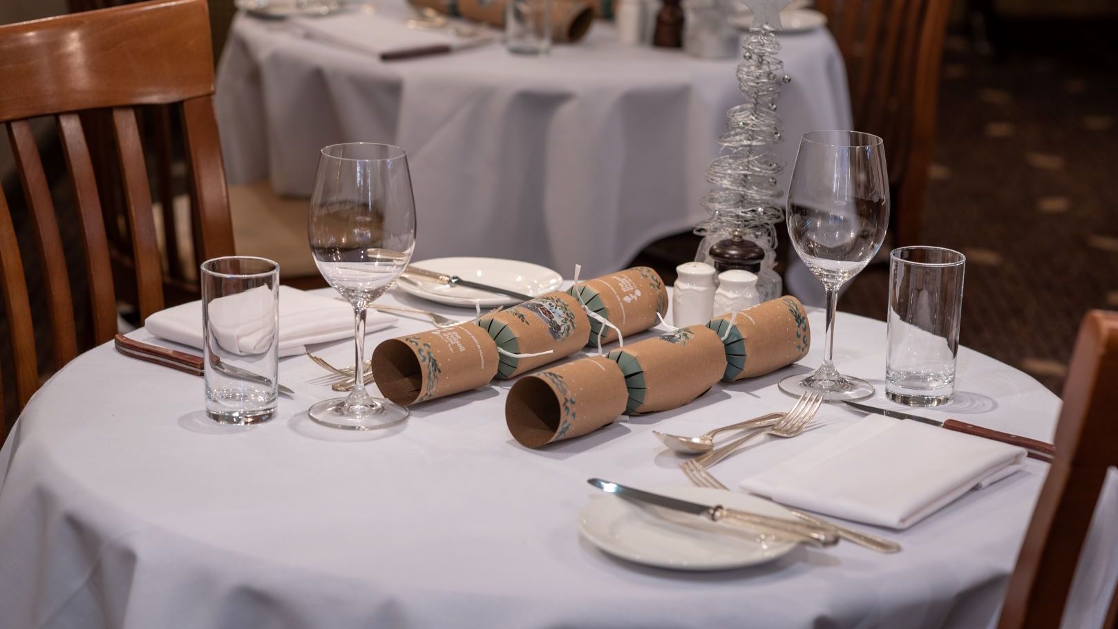 Elegant restaurant table setting with glasses, silverware, napkins, plates, and Christmas crackers