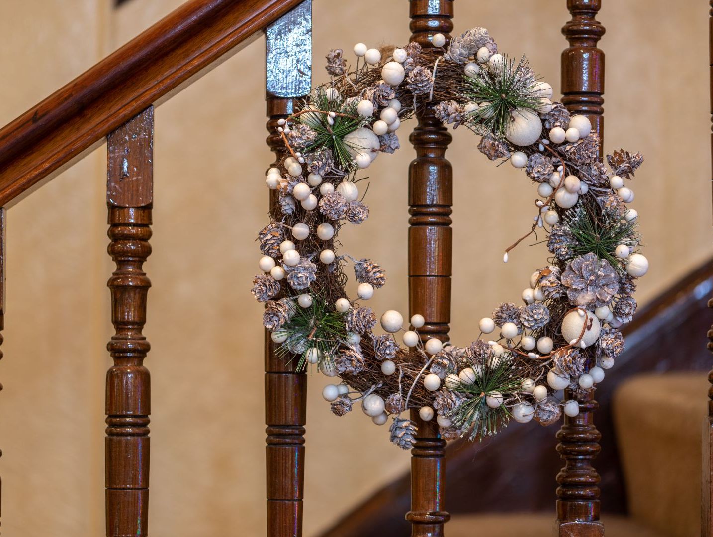 Festive wreath with pinecones and white berries hanging on a staircase railing