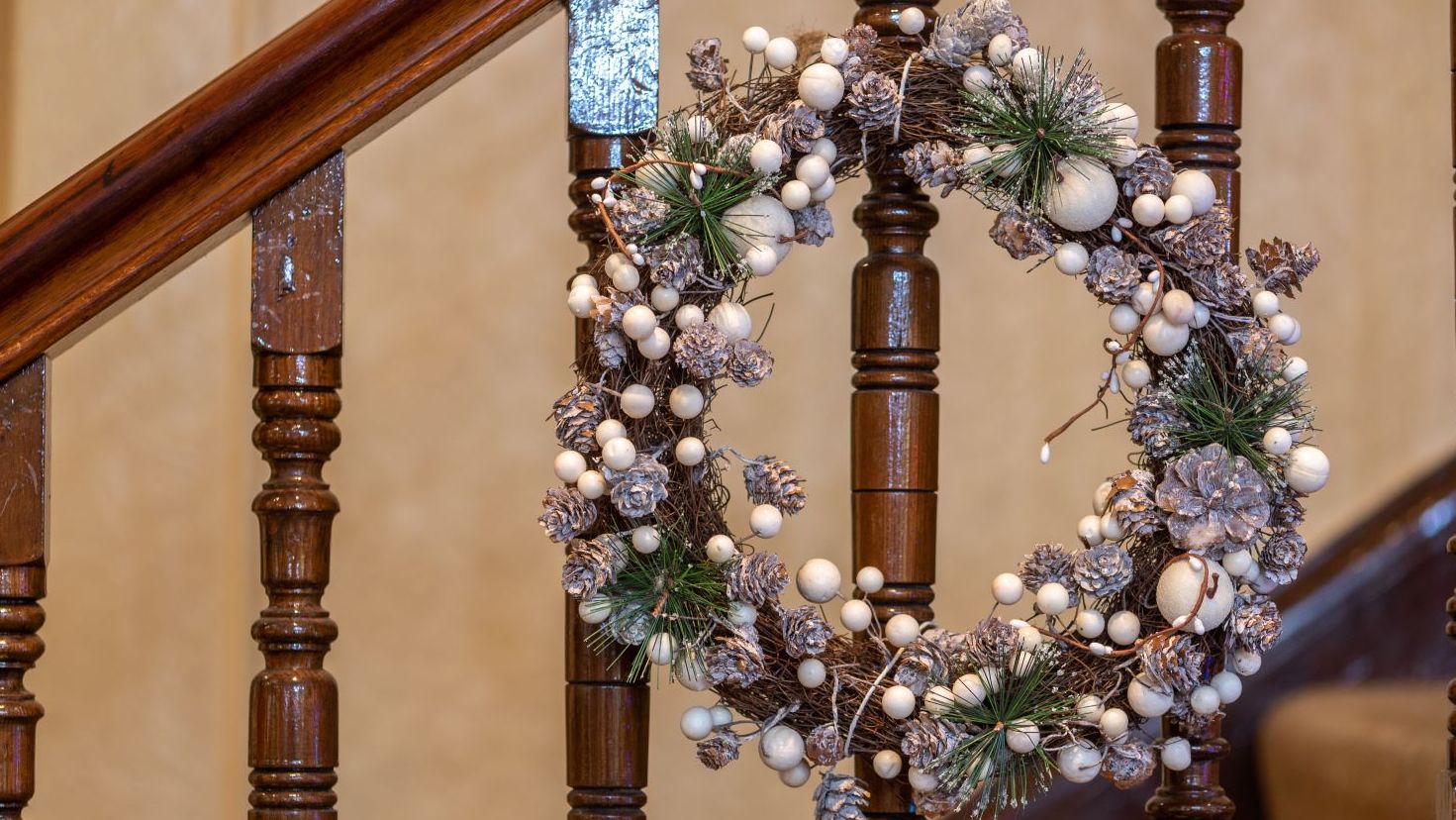 Festive wreath with pinecones and white berries hanging on a staircase railing