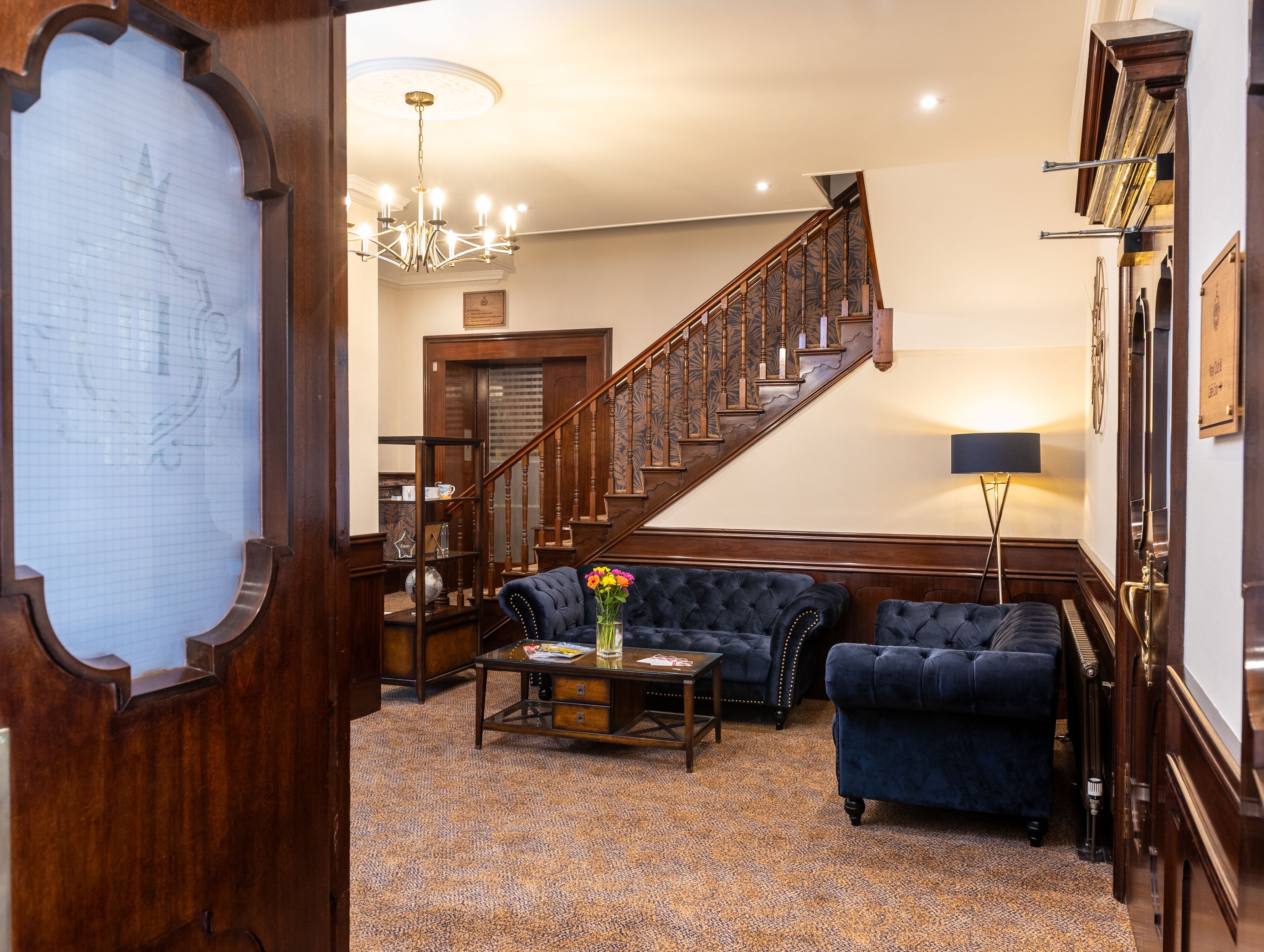 Hotel lobby with blue velvet sofas, wooden staircase, and chandelier