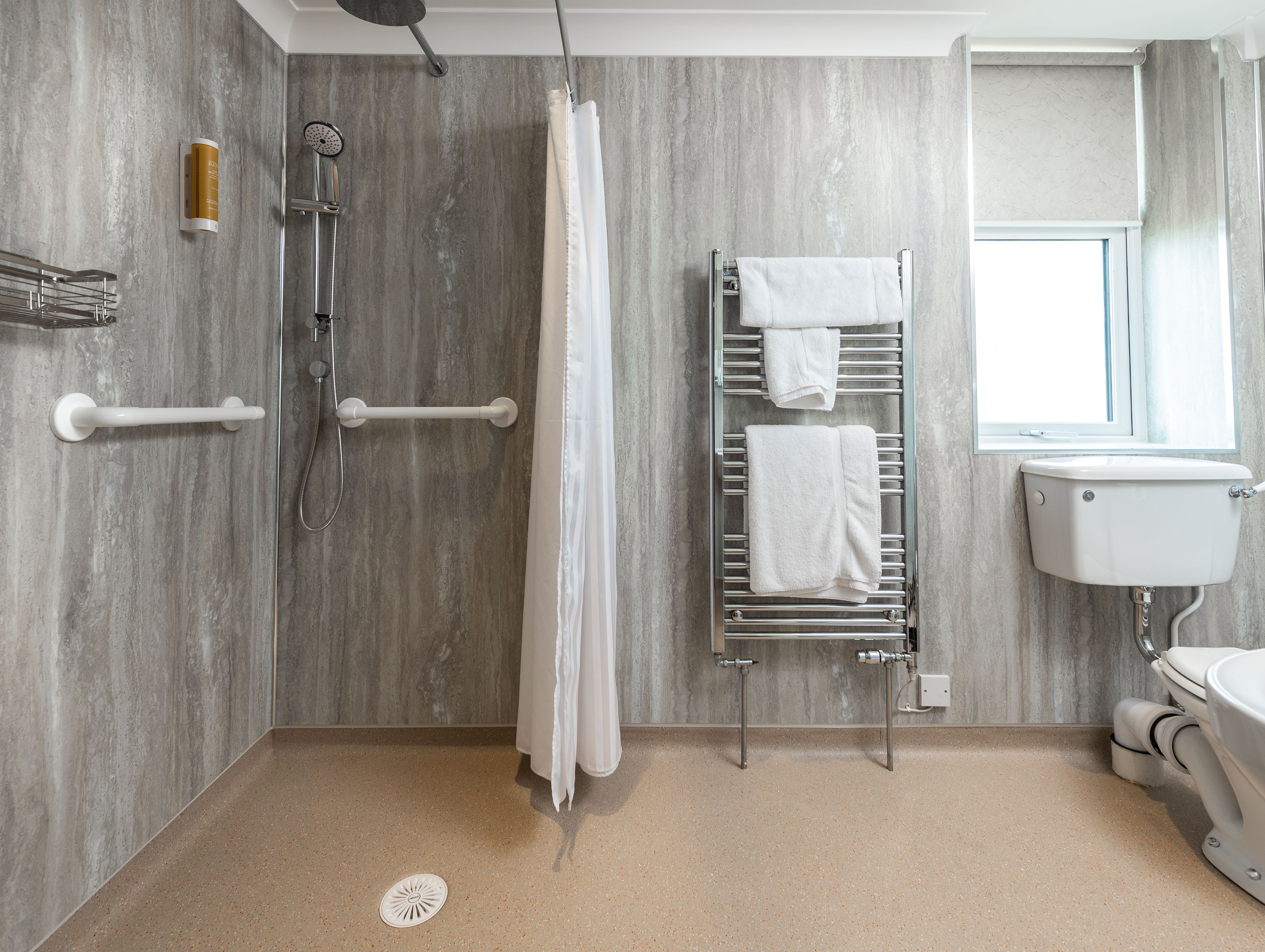 Accessible hotel bathroom with walk-in shower, grab bars, towel rack, and toilet.