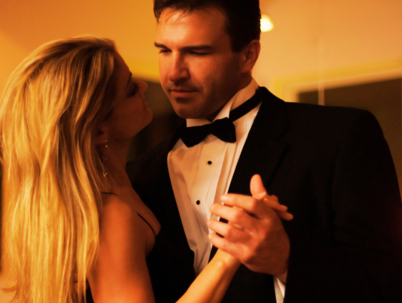 A couple elegantly dressed, slow dancing closely at an evening event.