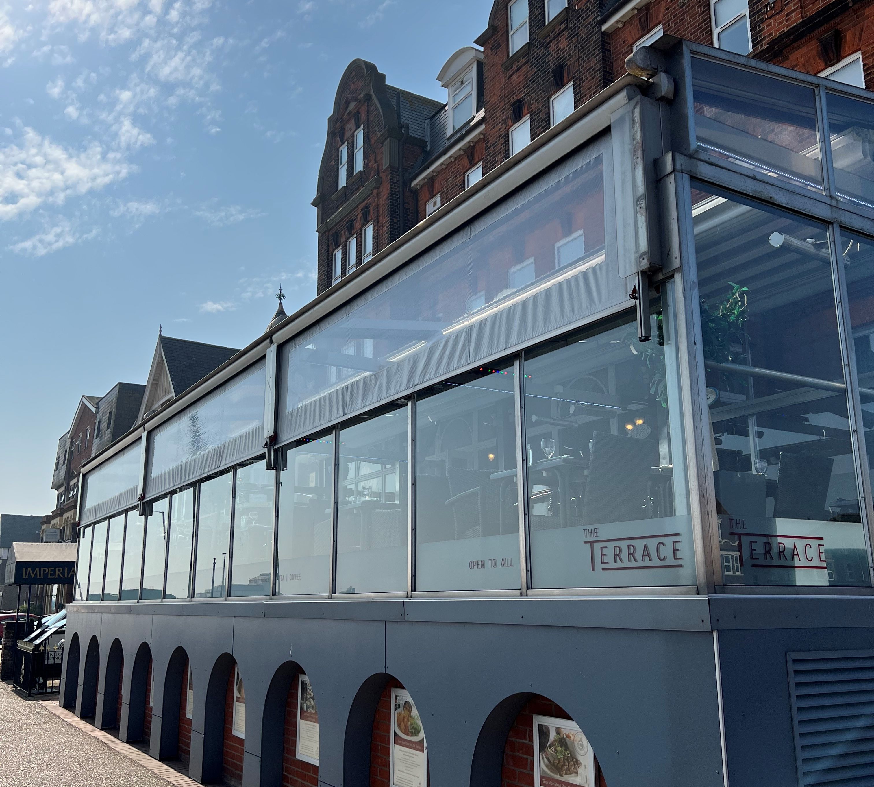 The Terrace at The Imperial Hotel with large windows and a traditional brick facade under a sunny sky.