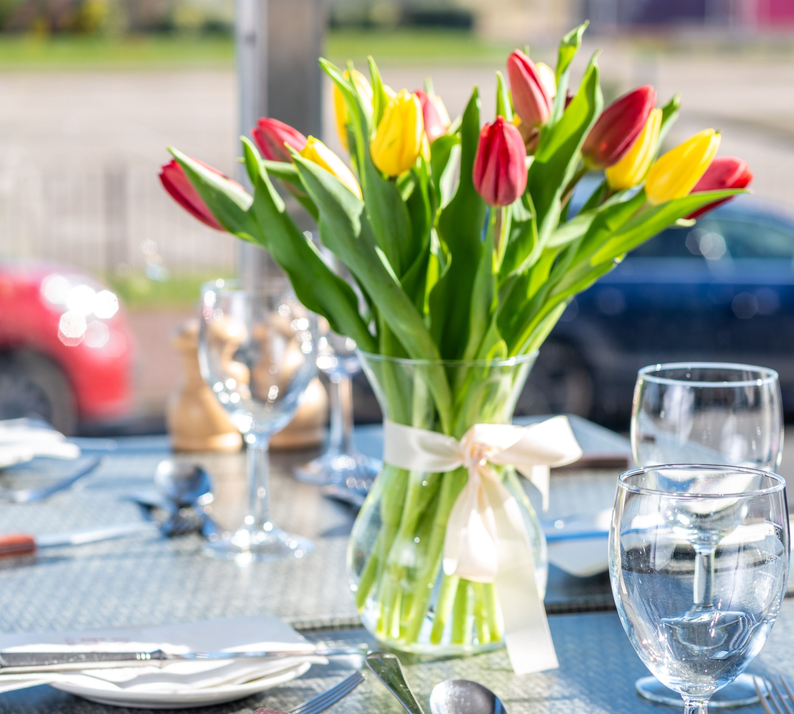 A dining table set with glassware, cutlery, a vase of red and yellow tulips, and a menu titled 'The Terrace'.