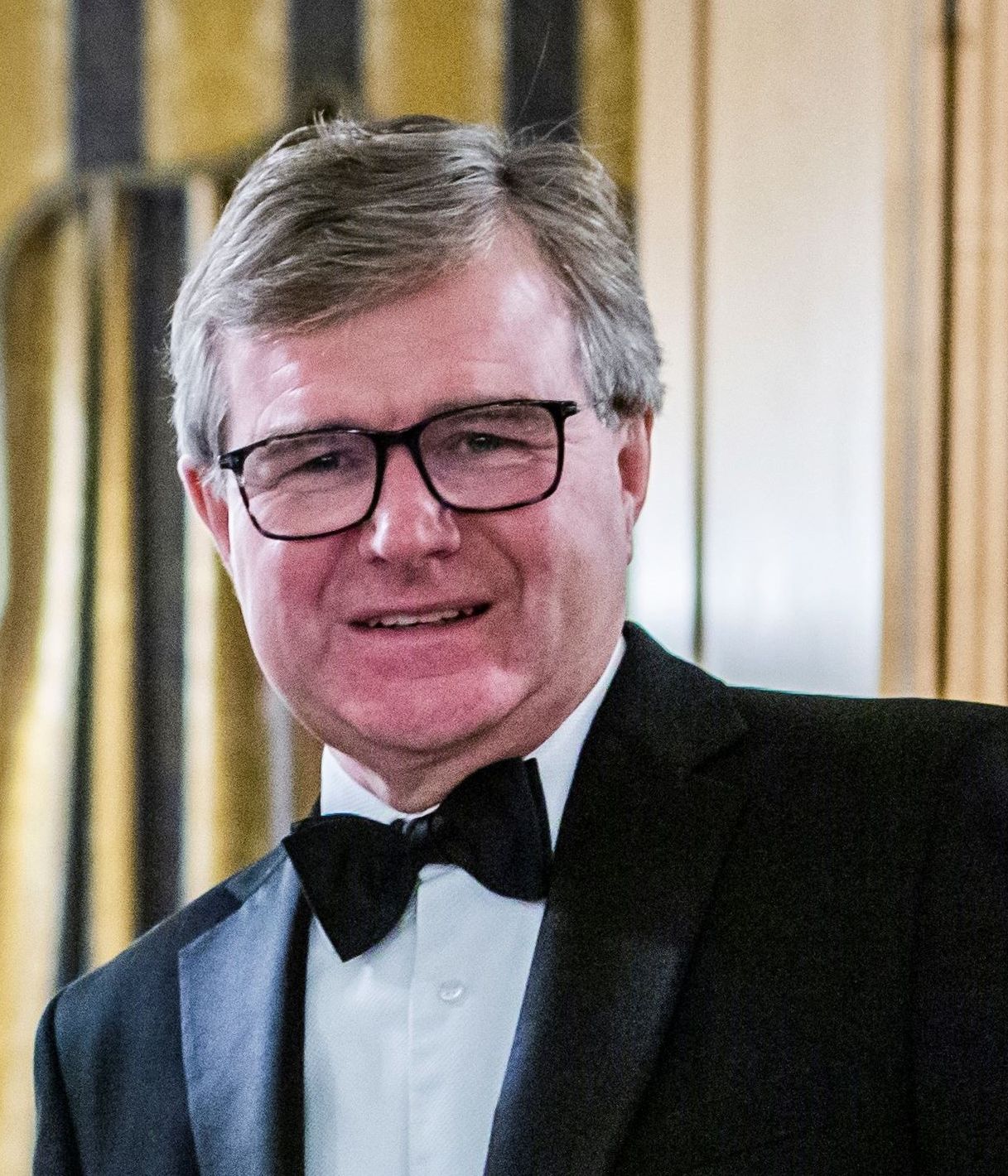 Man wearing glasses and a tuxedo with a bow tie, smiling at the camera.