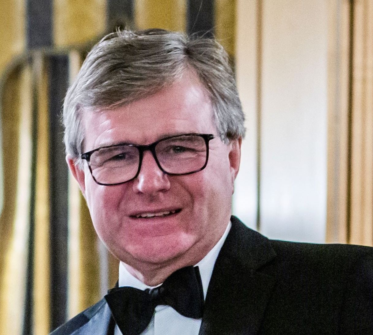 Man wearing glasses and a tuxedo with a bow tie, smiling at the camera.