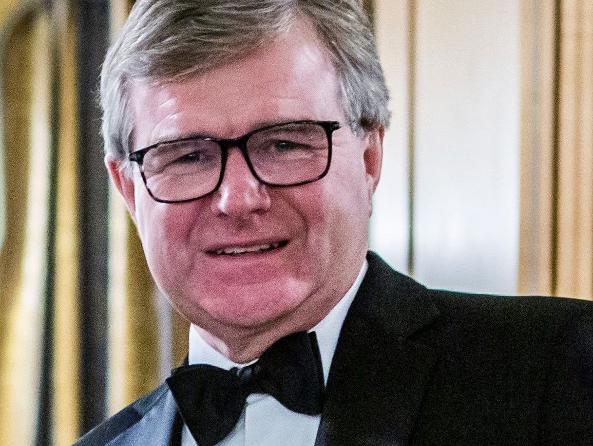 Man wearing glasses and a tuxedo with a bow tie, smiling at the camera.