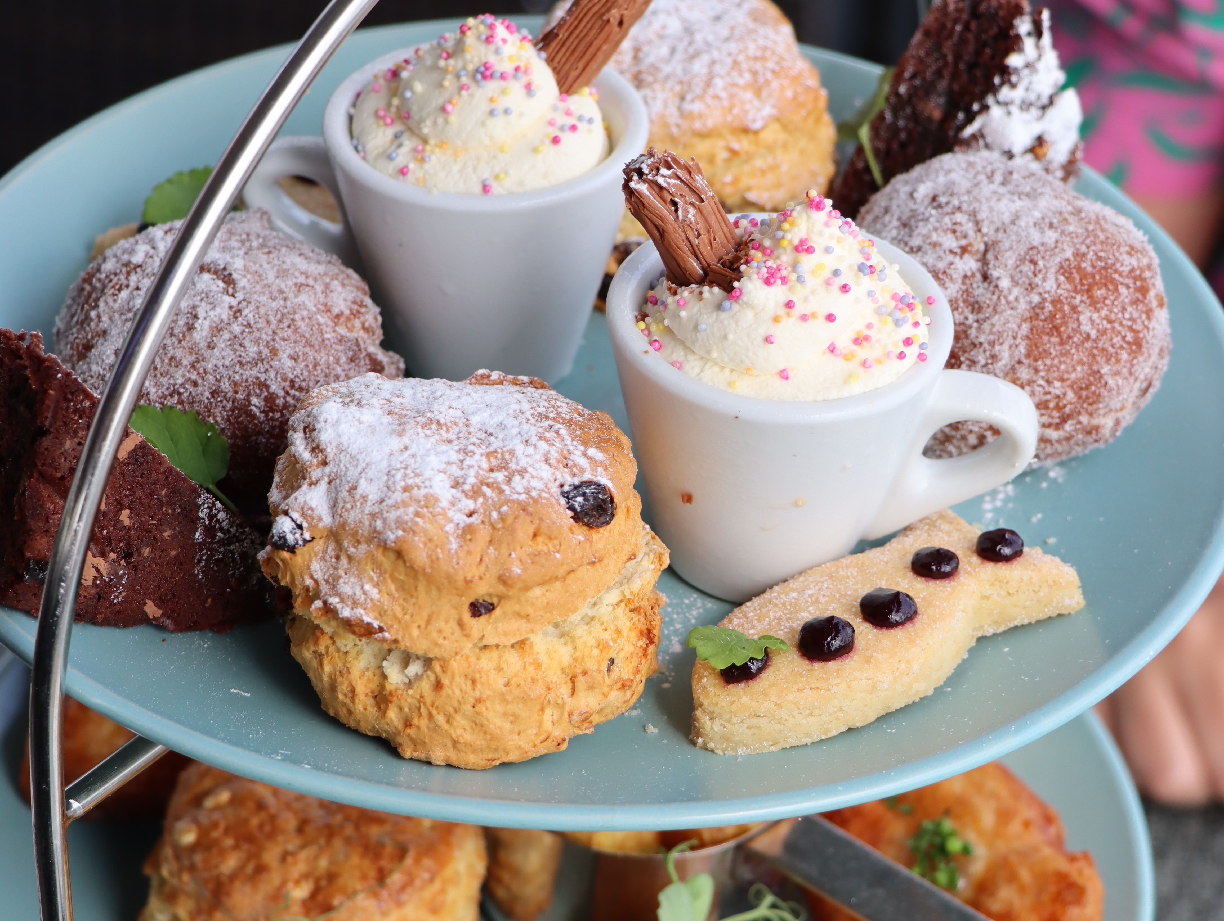 Afternoon tea stand with scones, doughnuts and mini cups of whipped cream topped with sprinkles