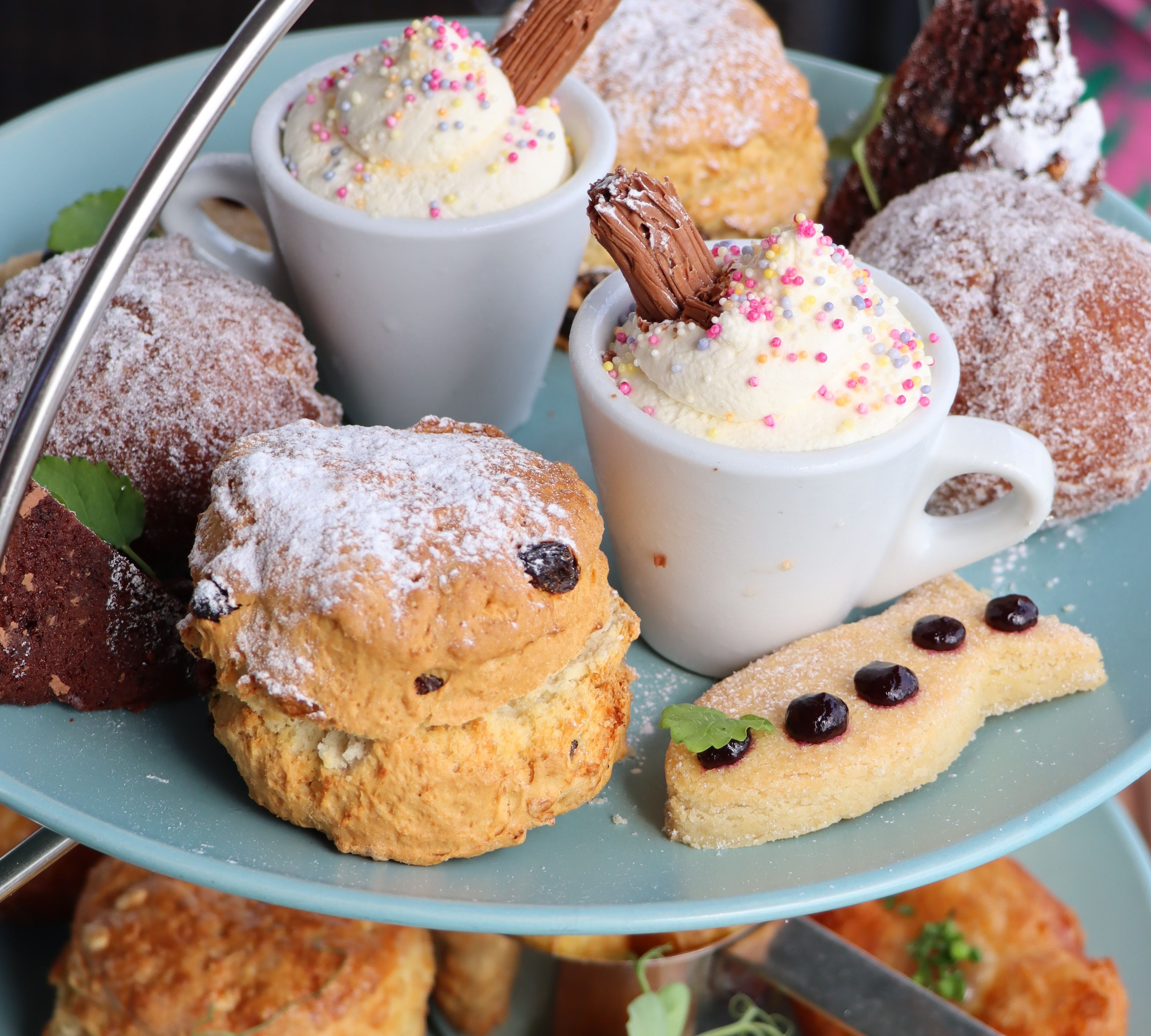 Afternoon tea stand with scones, doughnuts and mini cups of whipped cream topped with sprinkles