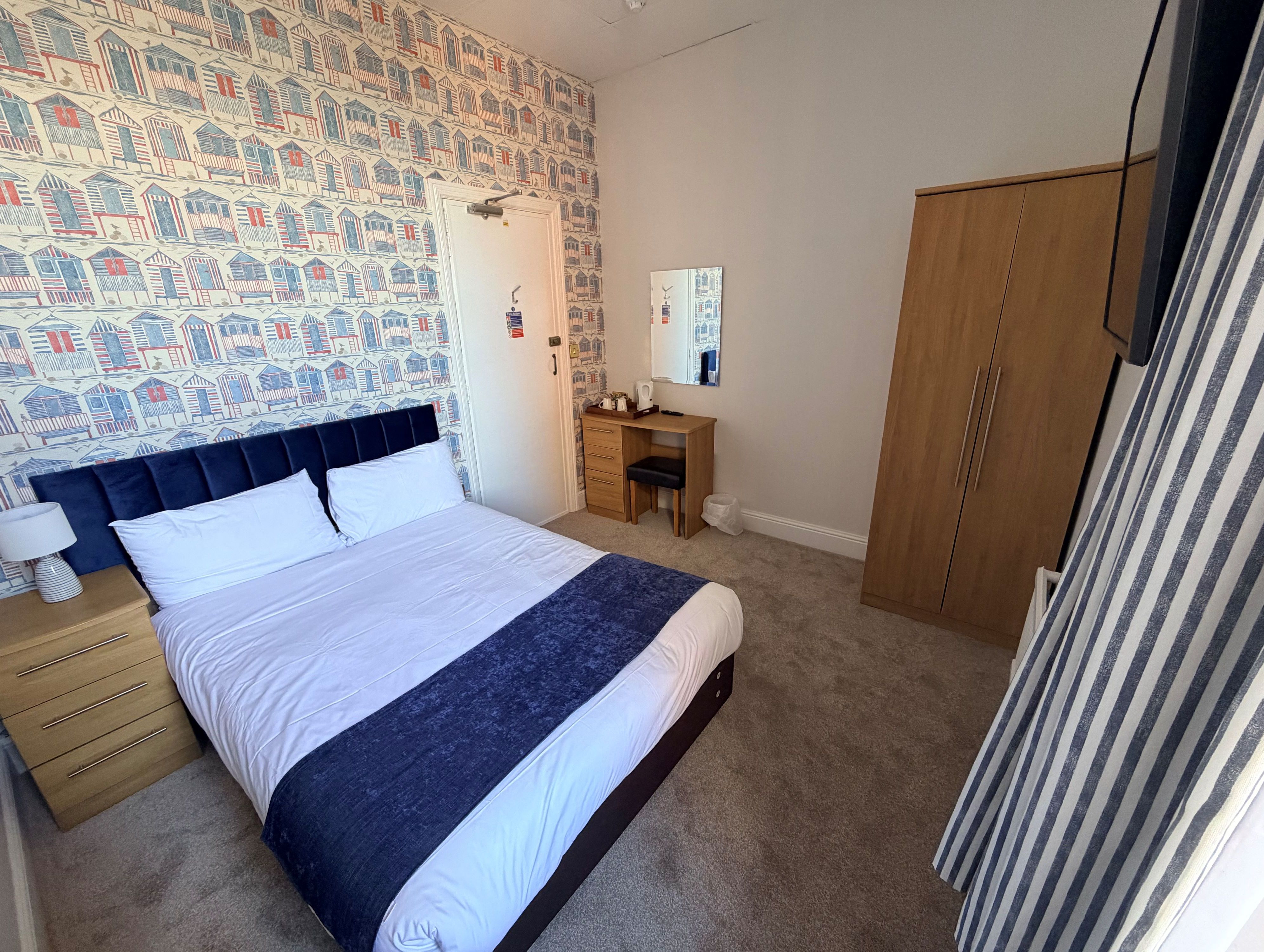 Double bedroom at Imperial Lodge, Great Yarmouth with blue headboard, seaside hut wallpaper, wardrobe and dressing table