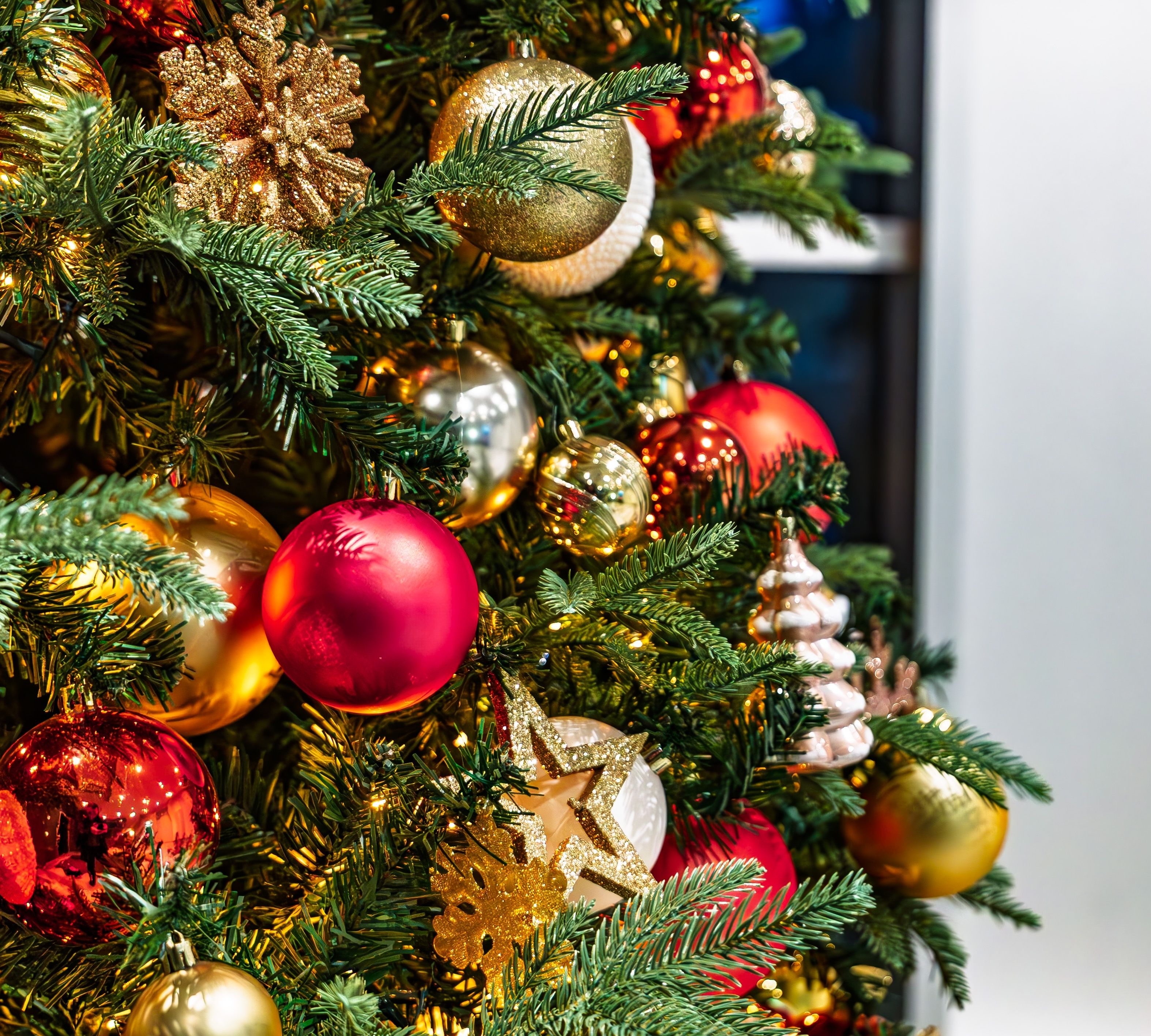 Close-up of a decorated Christmas tree with red and gold baubles, glittery snowflakes and warm fairy lights