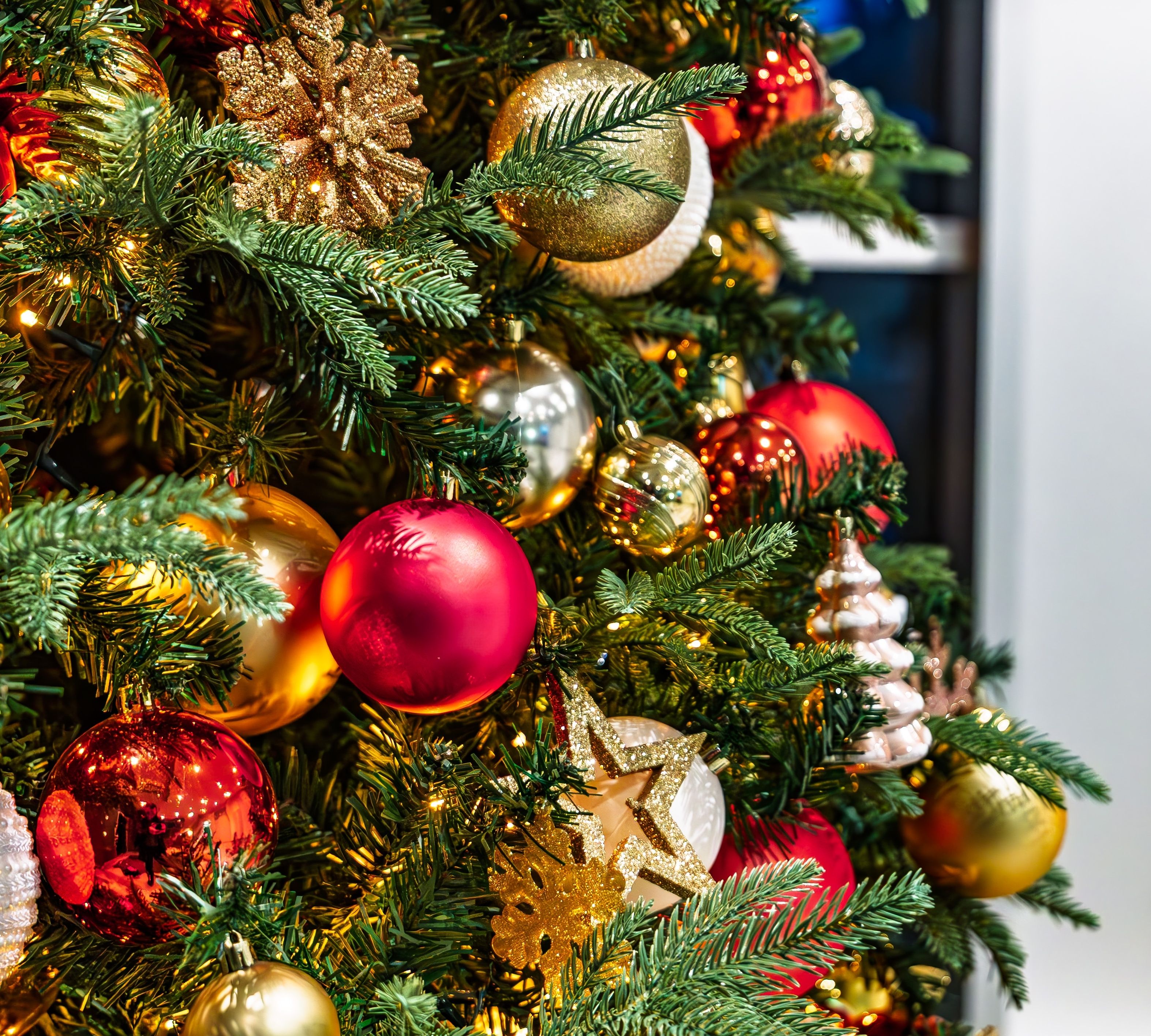 Close-up of a decorated Christmas tree with red and gold baubles, glittery snowflakes and warm fairy lights
