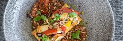 Beautifully plated gourmet vegetable dish topped with seeds and microgreens on a textured grey plate.