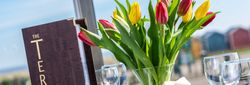 Table setting with a menu reading 'The Terrace' and a glass vase of red and yellow tulips