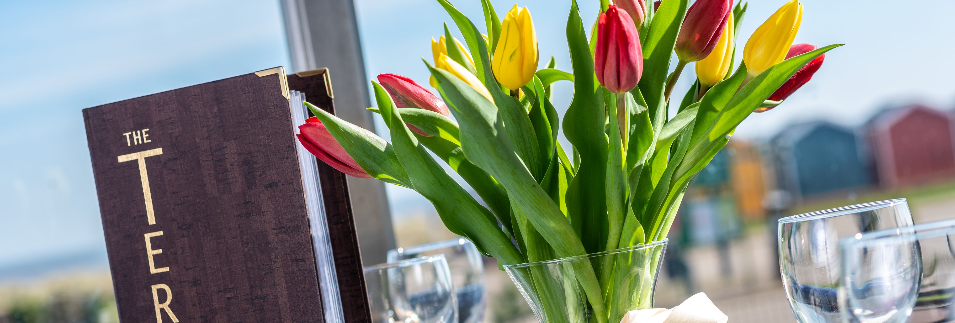 Table setting with a menu reading 'The Terrace' and a glass vase of red and yellow tulips