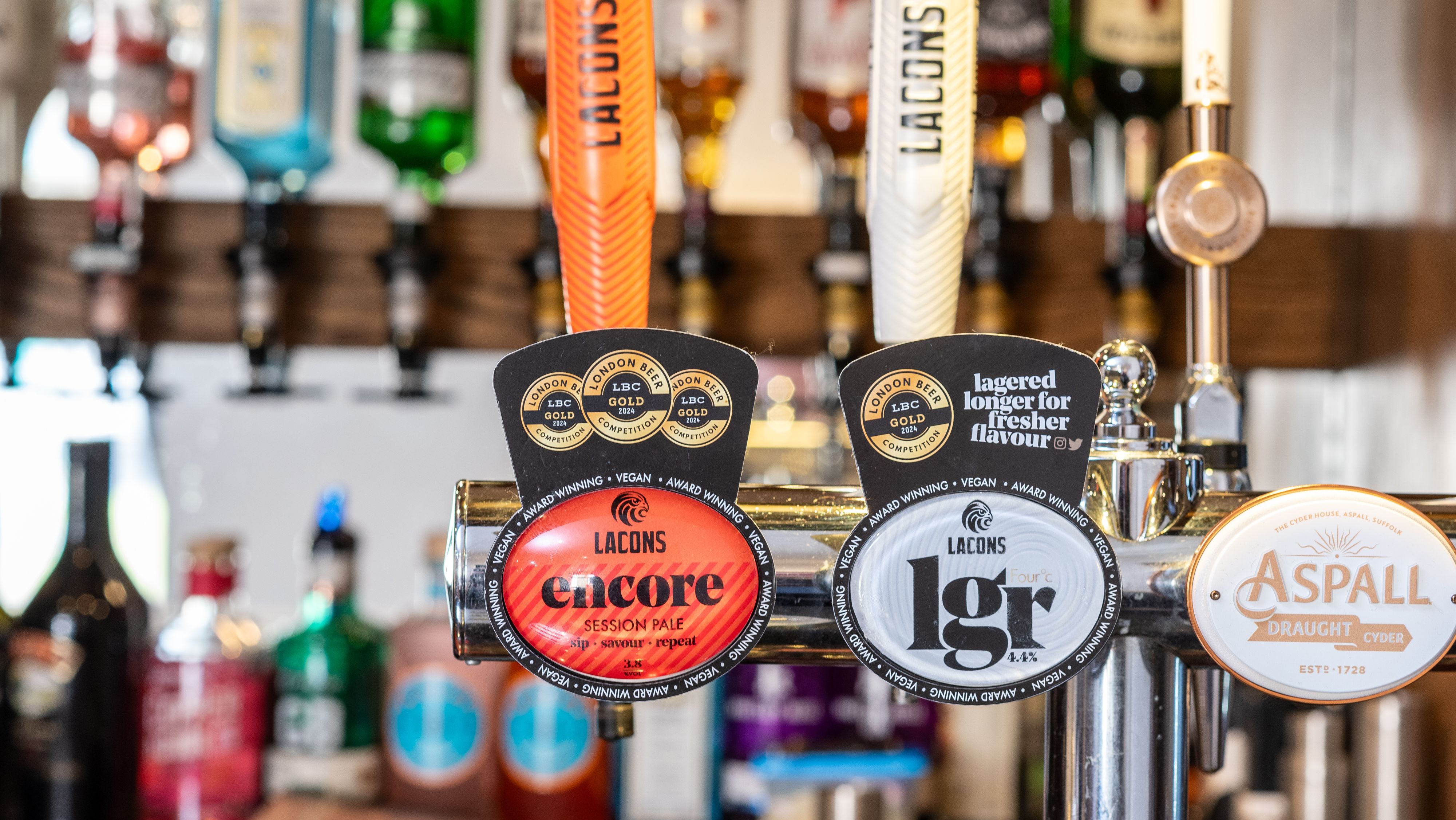 Close-up of beer and cider pumps at a bar with labels for Lacons Encore, Lacons LGR, and Aspall Draught Cyder.
