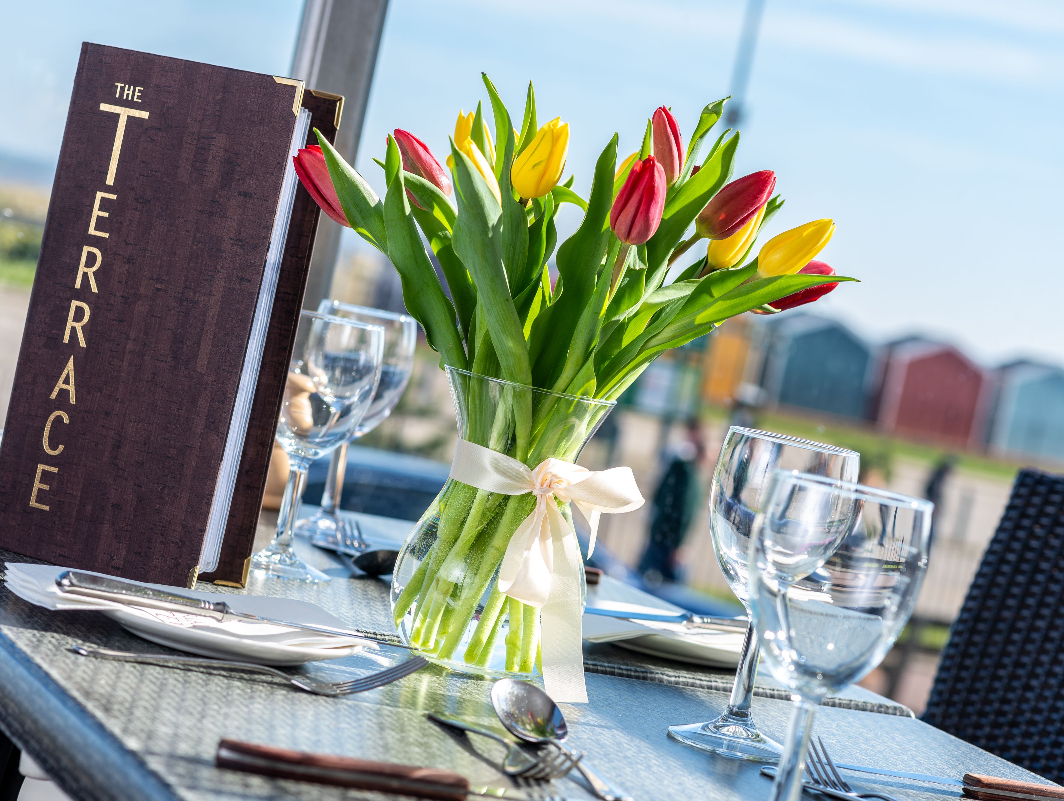 Vase of red and yellow tulips on a set restaurant table beside a 