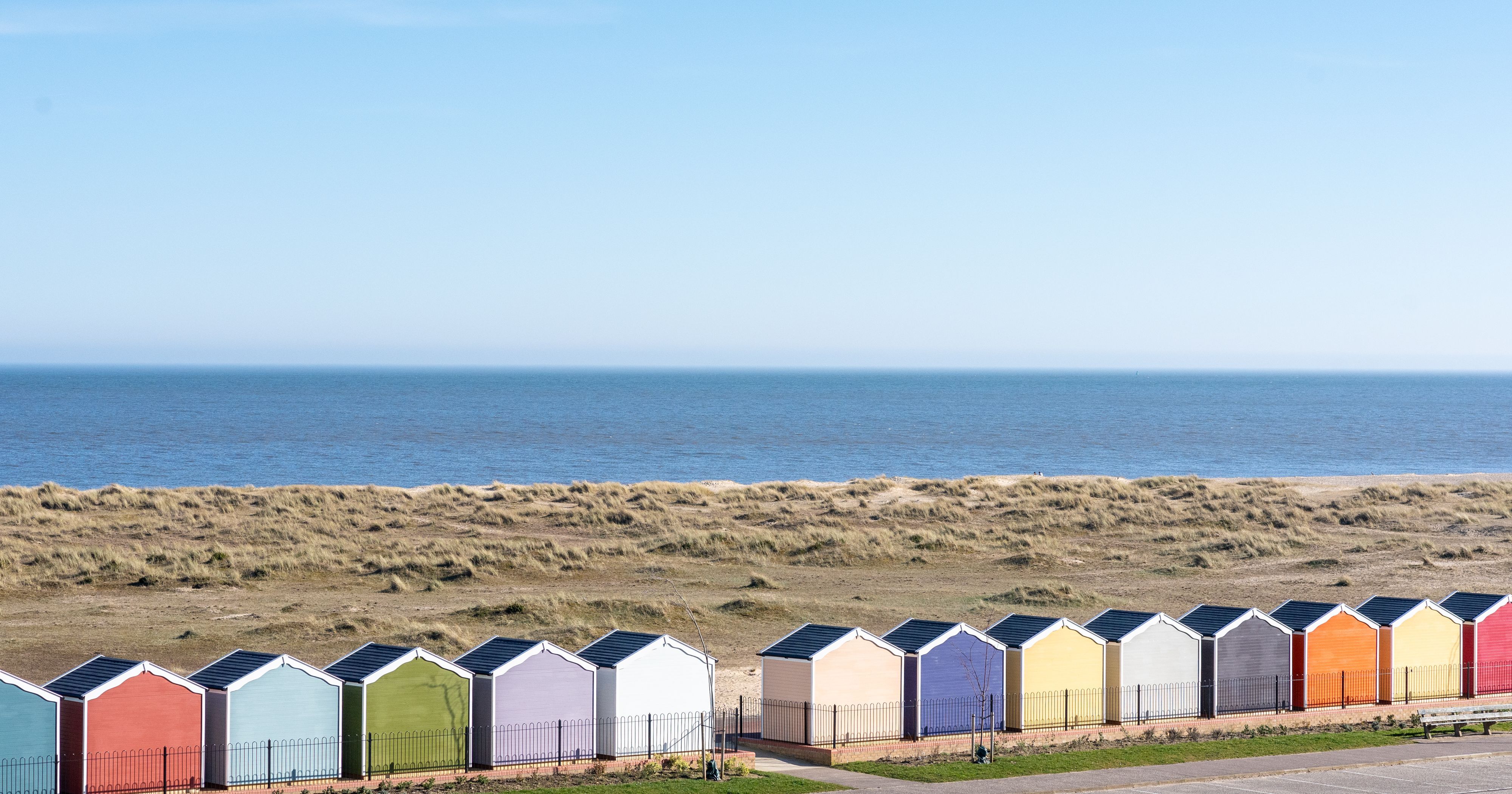 Row of colourful beach huts with the sea and blue sky in the background