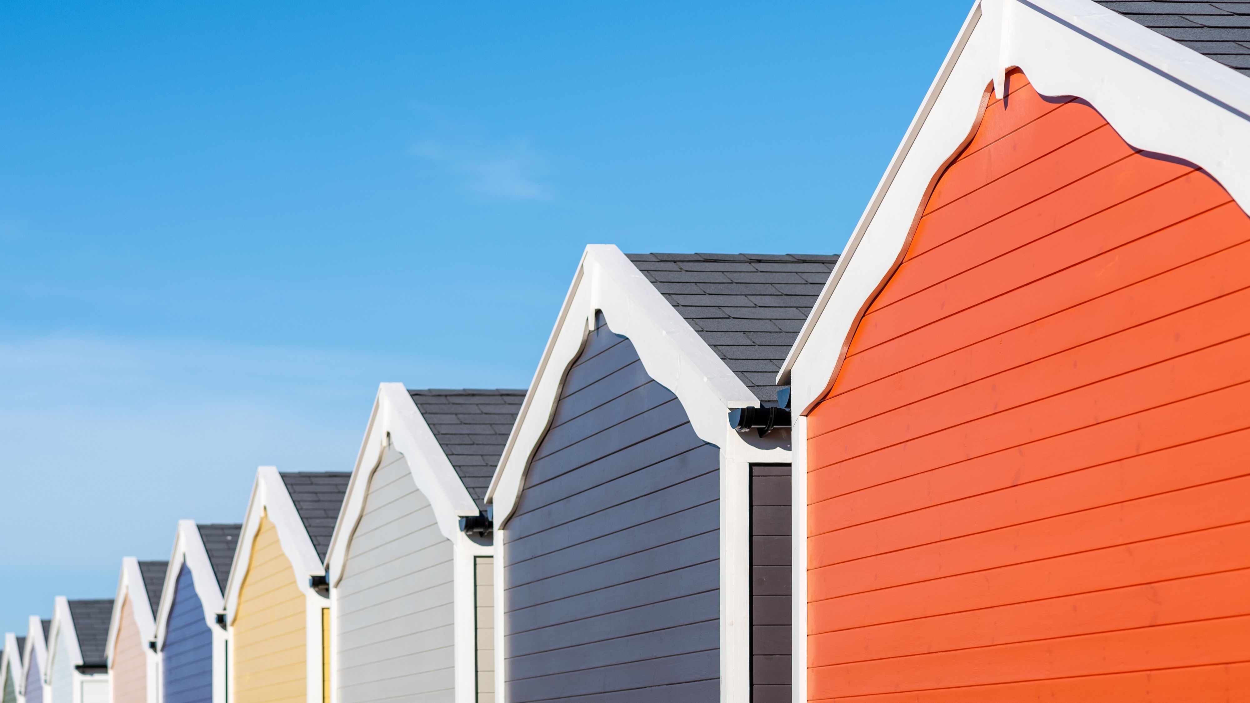 Row of colourful beach huts with pitched roofs against a clear blue sky