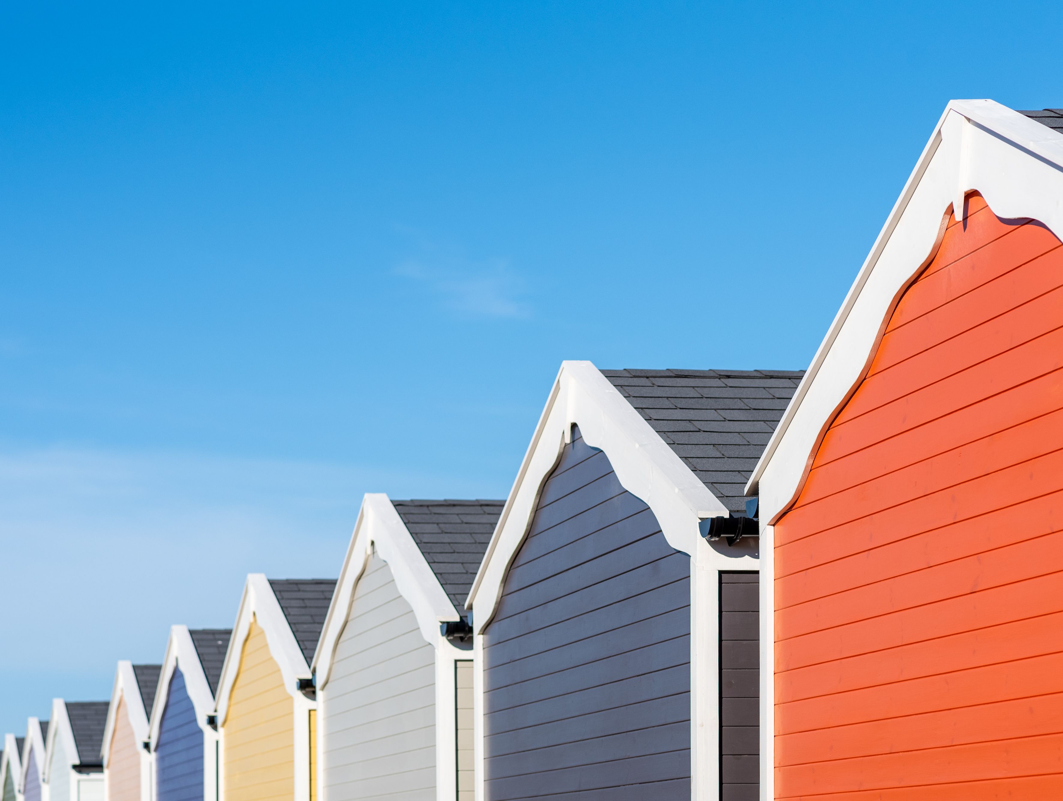 Row of colourful beach huts with pitched roofs against a clear blue sky