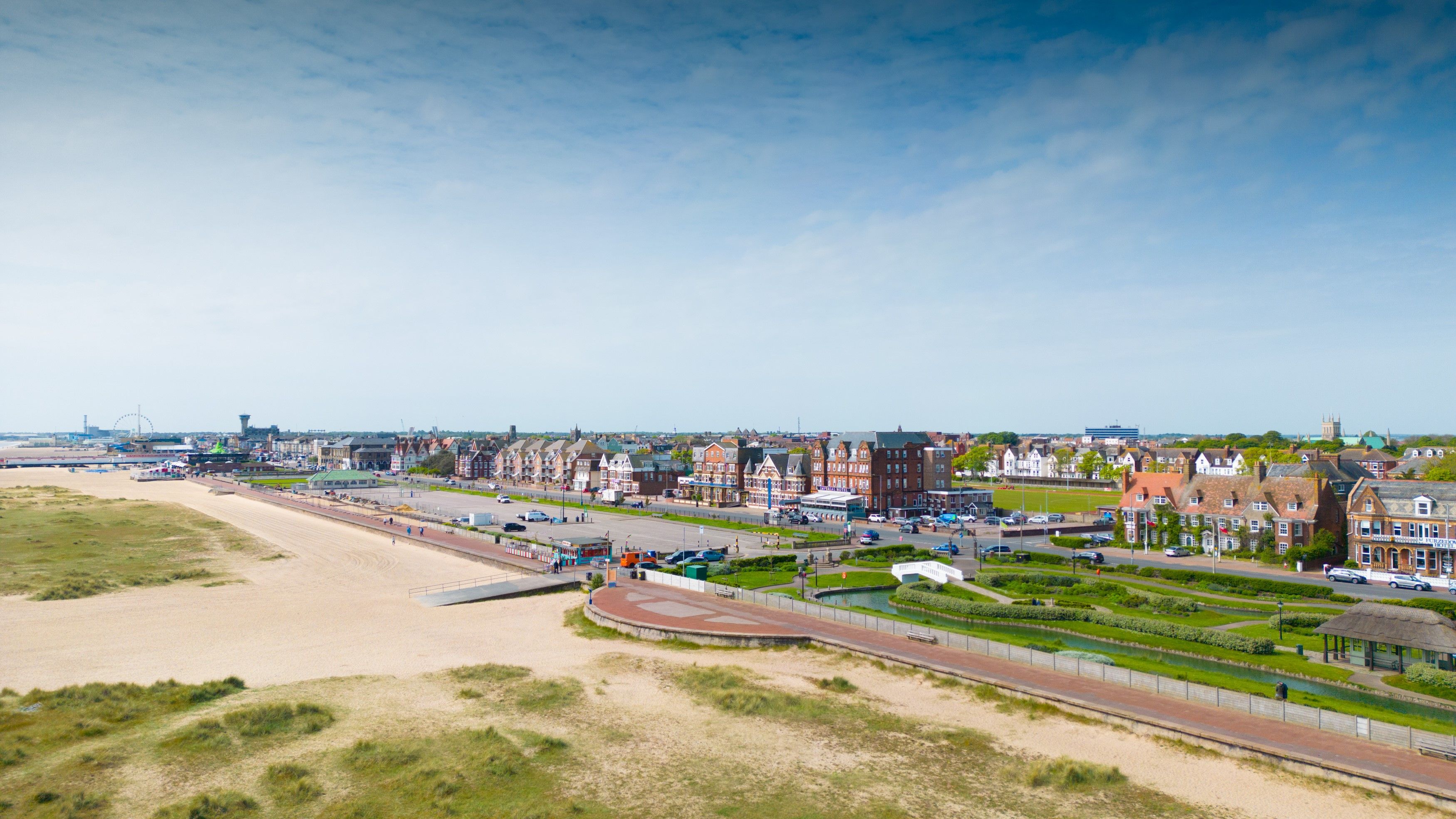 Panoramic view of a seaside town with sandy beach, promenade and rows of houses under a blue sky