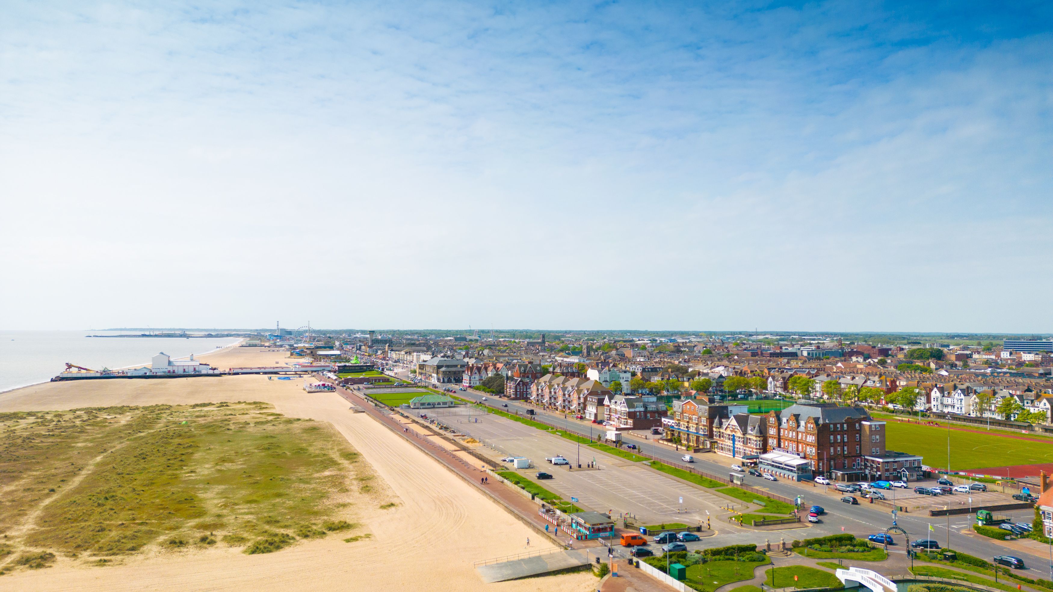 Aerial view of a seaside town with sandy beach, promenade and buildings under a blue sky