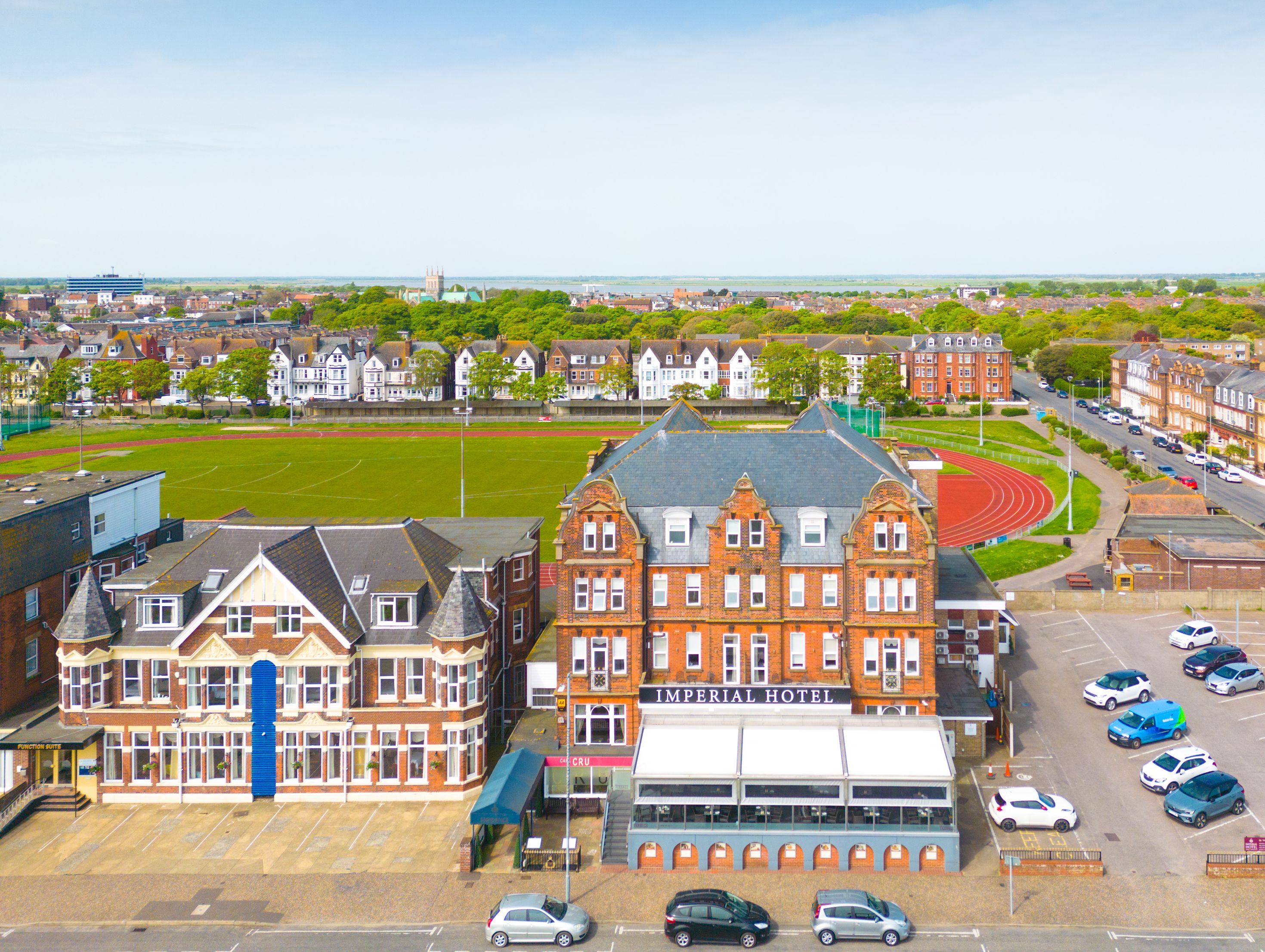 Aerial view of the Imperial Hotel beside a running track and sports field with a townscape under a blue sky