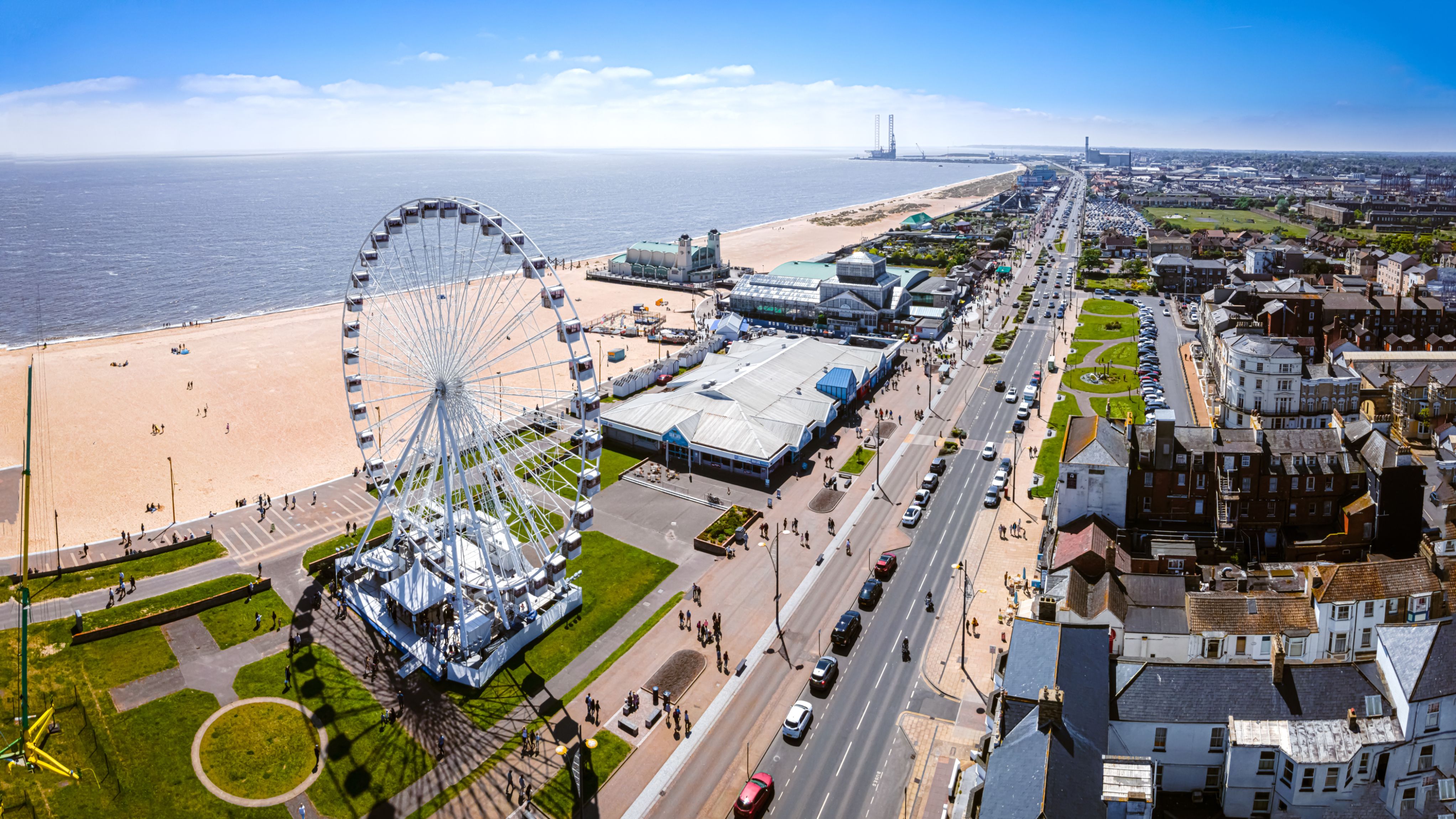 Aerial view of a seaside promenade with a large Ferris wheel beside a sandy beach and coastal town