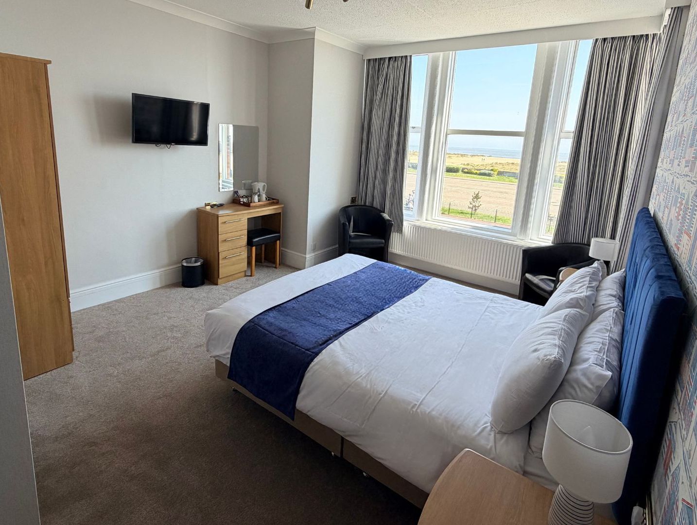 Bright double bedroom with blue headboard, large bay window and sea view