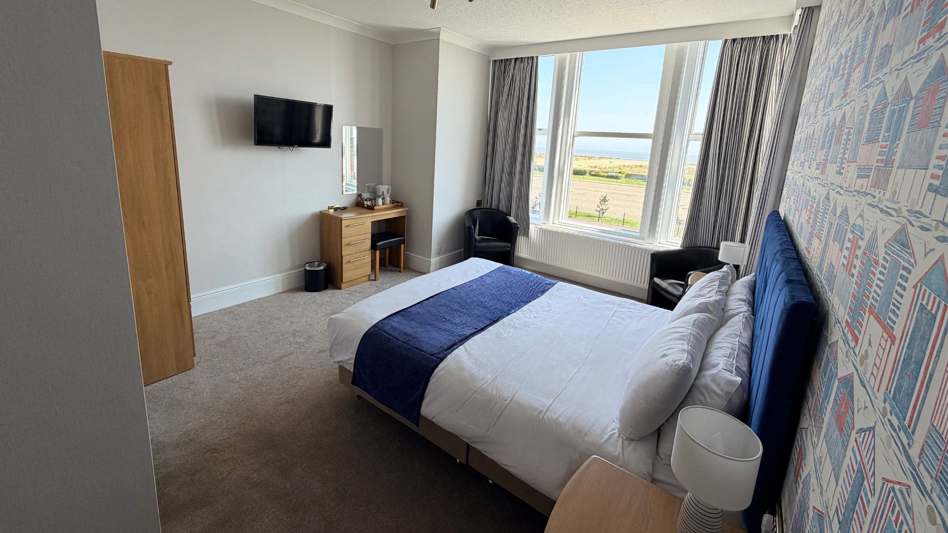 Bright double bedroom with blue headboard, large bay window and sea view