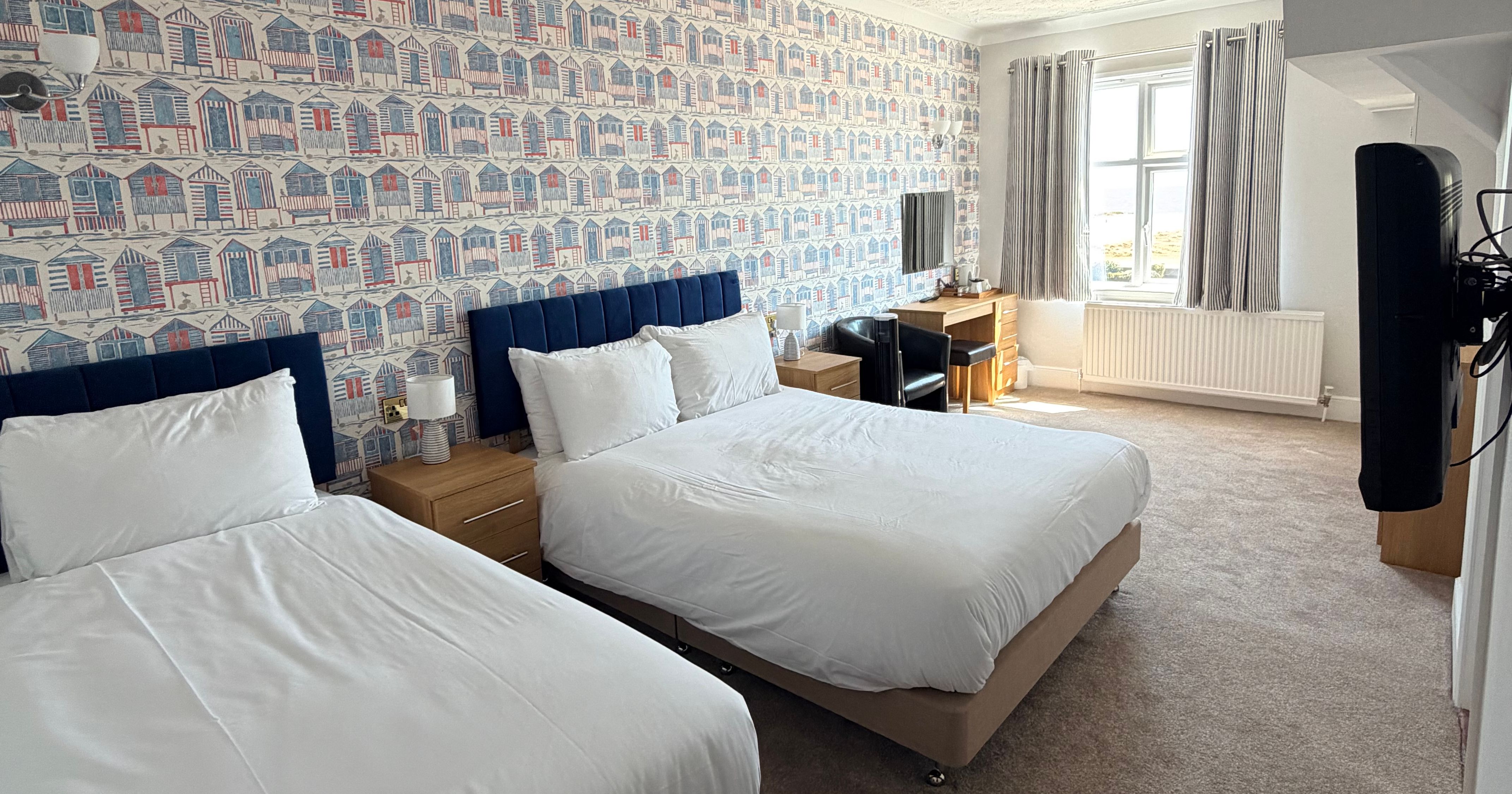 Twin bedroom with two single beds, seaside hut wallpaper and a window with a sea view