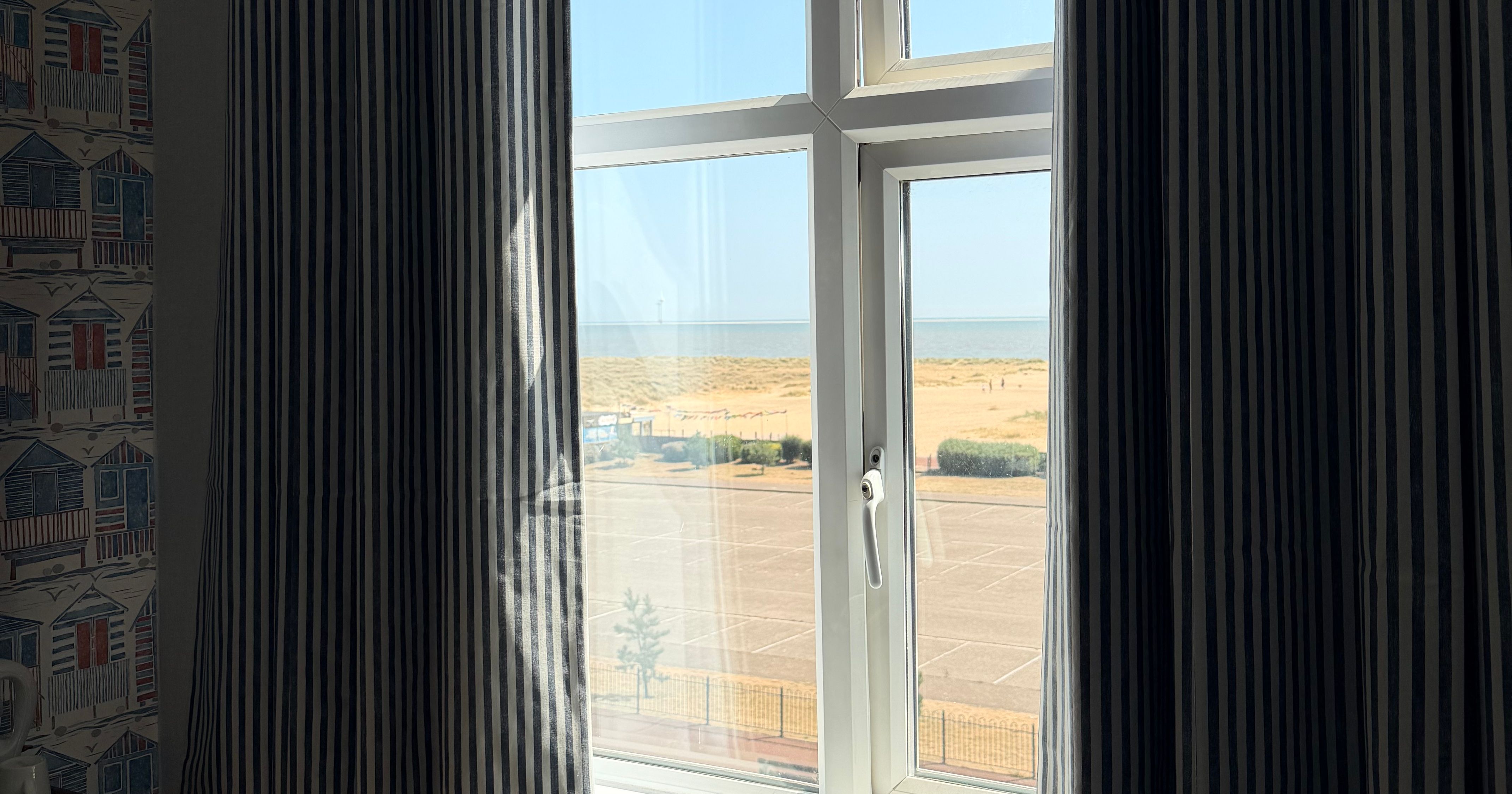 Striped curtains framing a window with a sea view over the beach