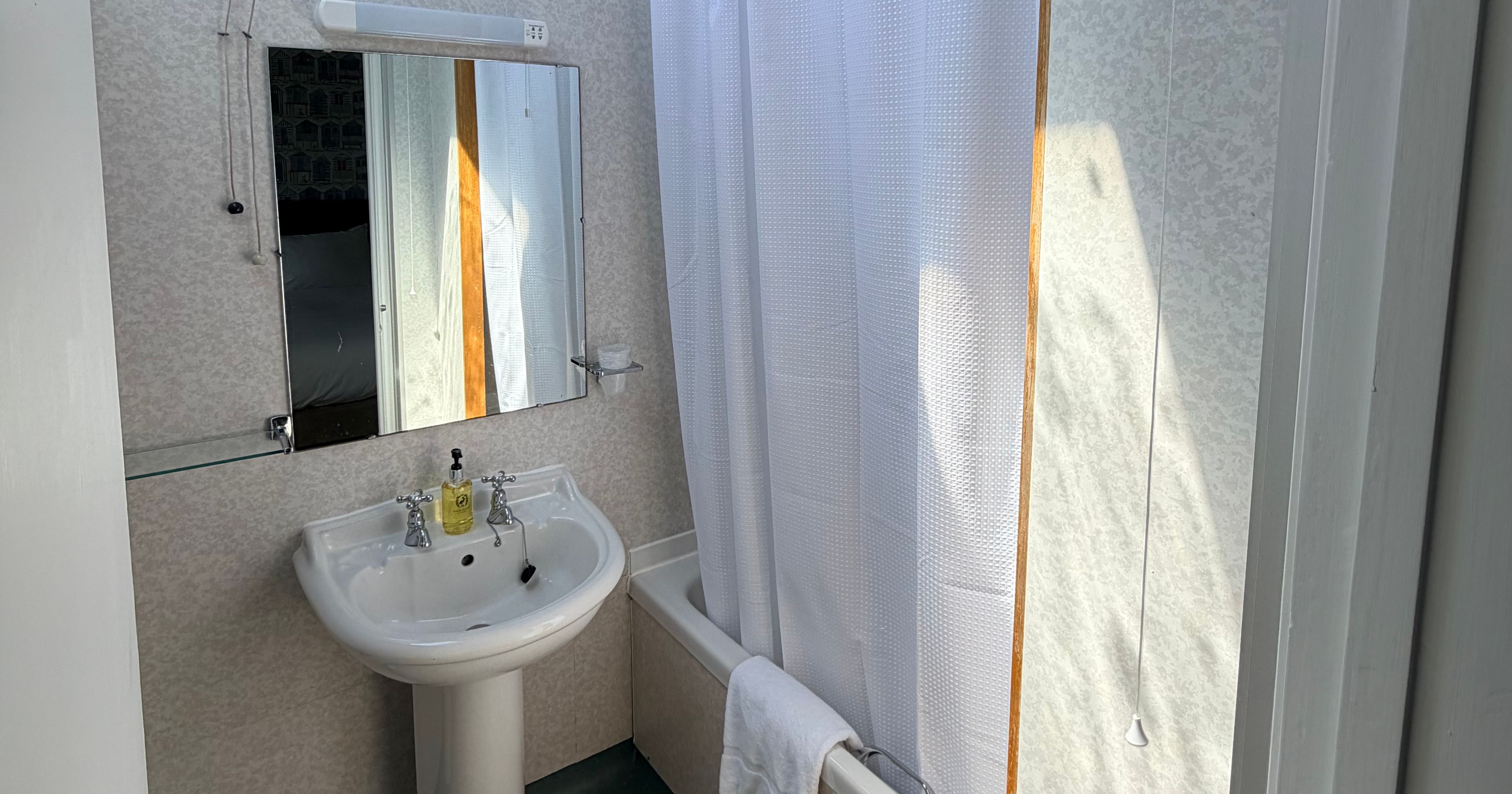 Compact lodge bathroom with pedestal sink, mirror and bath with white shower curtain