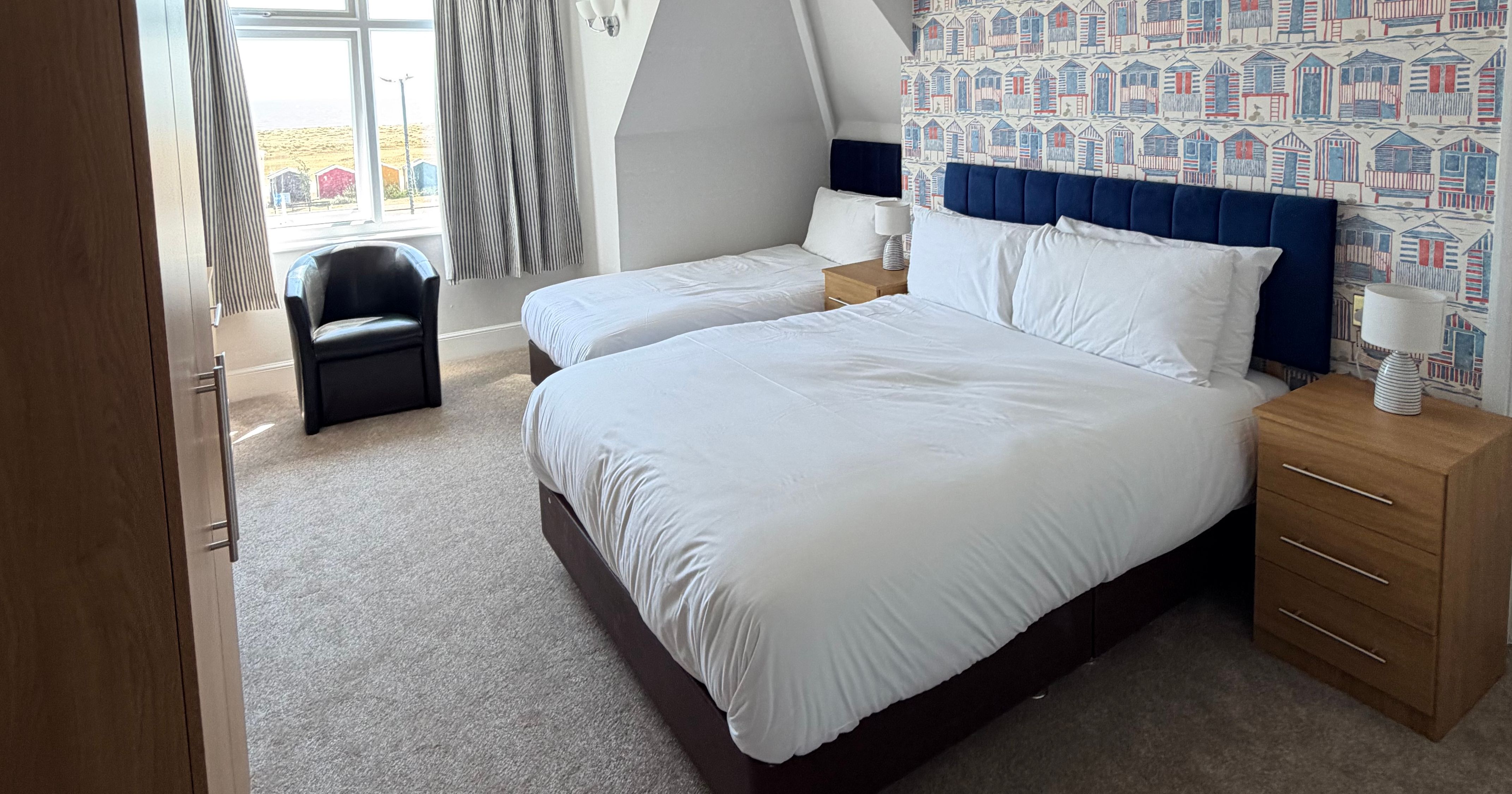 Twin bedroom with two single beds, seaside hut wallpaper and window with sea view